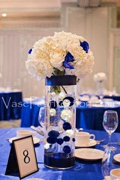 a vase with white and blue flowers is on a table set for an elegant dinner