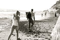 a man and woman walking on the beach next to each other with people in the background