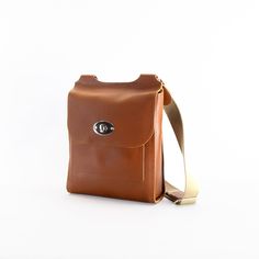 a brown leather bag with a metal handle on a white background and a tan strap around the shoulder