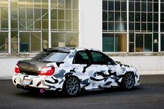 a white car with camouflage paint parked in front of a building