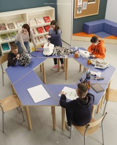 several children are sitting at tables in a room with bookshelves and toys on the floor