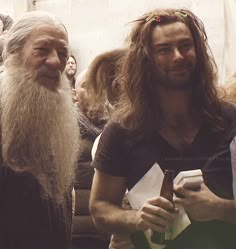 two men with long hair and beards standing next to each other in front of people