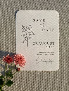 save the date card with pink flowers on it next to a white table cloth background