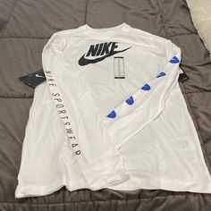 Nwt White Long Sleeve Nike Tee. The Left Sleeve Is Adorned With 5 Blue And White Nike Swoosh Emblems And The Right Arm Has Nike Sportswear Written Down It. The Back Of The Shirt Has The Nike Emblem Written Backwards. White Long Sleeve Sportswear T-shirt, Nike Long Sleeve Cotton T-shirt, Sportswear Long Sleeve T-shirt With Graphic Print, Sporty Long Sleeve T-shirt For Spring, Nike Long Sleeve T-shirt For Spring, Long Sleeve Cotton Sportswear T-shirt, Sports Long Sleeve Shirt With Letter Print, Sportswear Long Sleeve Tops With Letter Print, Long Sleeve Sports Shirt With Letter Print