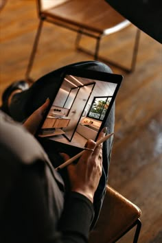 a person sitting in a chair holding an ipad with a house on it's screen