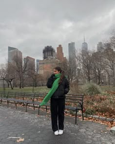 a woman standing in front of a park bench with a green scarf around her neck