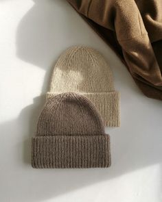 two hats are laying next to each other on a white surface with a brown coat in the background