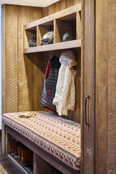 a wooden bench sitting inside of a room next to a wall filled with shoes and coats