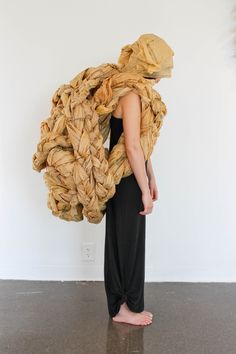 a woman standing in front of a white wall holding a large piece of cloth over her head