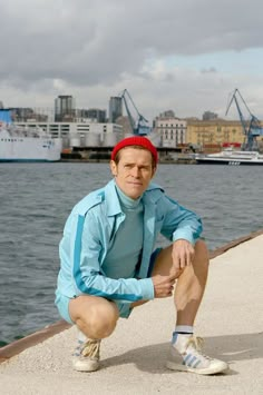 a man sitting on the edge of a pier next to water with boats in the background