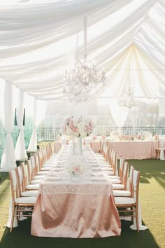 a long table set up for a formal event with chandelier and flowers on it