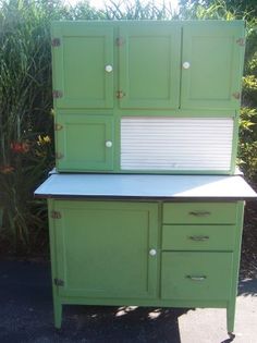 an old green cabinet with two doors and drawers sitting on the side of a road