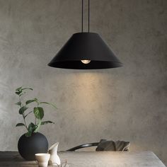 a black lamp hanging over a table next to a vase with a plant in it