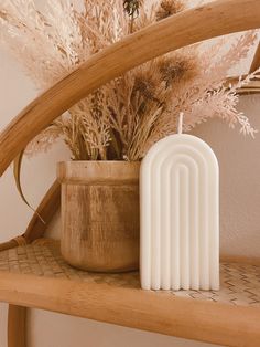 a white candle sitting on top of a wooden shelf next to some dried plants and reeds