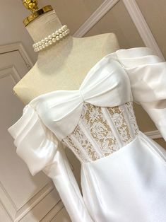 a white dress with gold details on the bustle and neckline is displayed in front of a mannequin