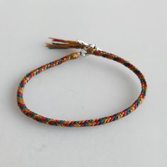 a multicolored bracelet with a silver clasp and tassel on the end, sitting on a white surface