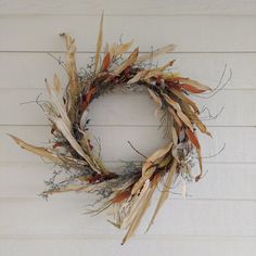 a dried wreath hanging on the side of a white house with grass and twigs around it