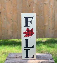 a wooden sign with the word fall painted on it in black and red, sitting on top of a piece of wood