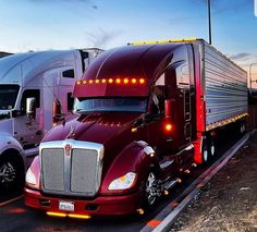 two semi trucks parked next to each other on the side of the road at sunset