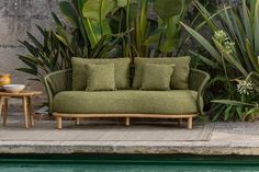 a green couch sitting next to a pool in front of a stone wall and plants