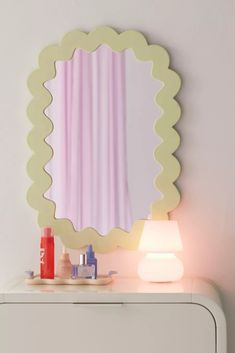 a white dresser topped with a mirror next to a lamp and bottle on top of it