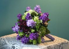 a bouquet of purple and green flowers sits on a lace covered tablecloth in front of a blue wall