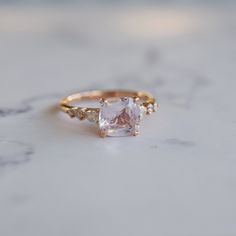 an engagement ring with a square cut diamond and three small diamonds around the band on a marble surface