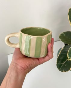 a hand holding a green and white striped coffee cup next to a potted plant