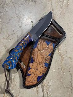 a knife is laying on top of a leather sheath with blue and gold designs,