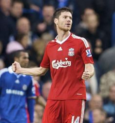 a man in red soccer uniform standing on a field with his arms out and people watching