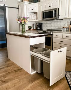 a kitchen with white cabinets and an island that has two trash cans in the middle