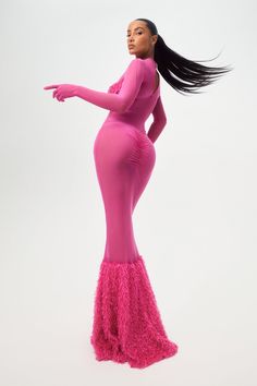 a woman in a pink dress with long black hair pointing to the side while standing against a white background