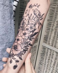 two people holding each other's hands with tattoos on their arms and flowers on the arm