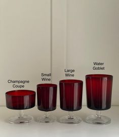 four wine glasses with names on them sitting next to each other in front of a white wall