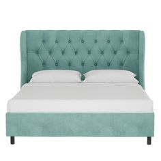 an upholstered bed with white pillows and green velvet headboard, viewed from the side