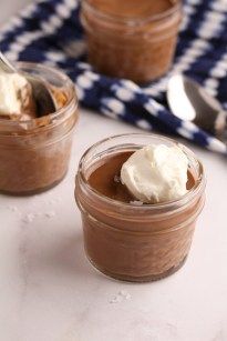 two small jars filled with pudding on top of a white tablecloth next to spoons