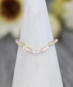 a gold ring with three small white stones sitting on top of a wooden table next to a flower