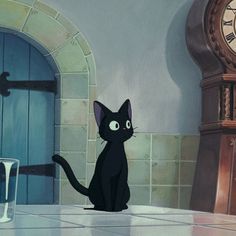 a black cat sitting in front of a clock