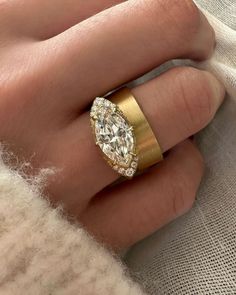 a woman's hand wearing a gold ring with an oval shaped diamond in the center