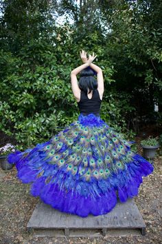 a woman in a black top and blue peacock skirt sitting on a bench with her hands up