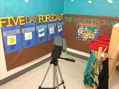 a classroom room with a weather chart on the wall and a tripod in front of it