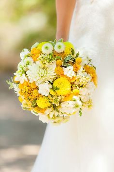 a bride holding a bouquet of yellow and white flowers