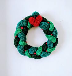 a green and red knitted christmas wreath on a white surface with a red heart