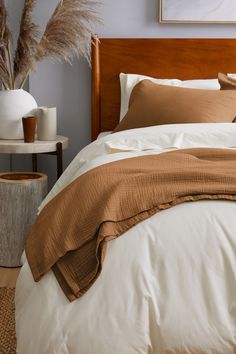 a bed with brown and white comforters in a bedroom next to a vase filled with dry grass