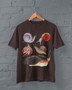 Thanks for stopping by! Cottagecore Snails T-shirt Printed on a super soft, cotton tee Dispatched in 5 working days or sooner Unisex Free UK delivery Material: 100% ringspun cotton. Chest (to fit): S  34/36   M  38   L  40/42   XL  44/46   XXL  48/50 ECO-FRIENDLY Each garment is made to order, reducing extra material and energy that would be otherwise wasted We use DTG printing process which is easier on the environment than screen-printing Our ink is bright and also eco-friendly. Do not tumble Different Aesthetic Clothes, Goblincore Goth, Art On T Shirt, Bug Clothes, Goblincore Shirt, Goblincore Fashion, Fairycore Clothing, Bug Shirt, Brown Shirts