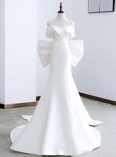 a white wedding dress on display in a room with a mannequin behind it