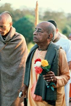 an old man with a flower in his hand standing next to another man wearing a shawl