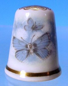 a small bell with a blue butterfly painted on it's side and gold trim around the bottom