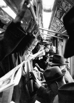 black and white photograph of people sitting on a bus reading newspapers while others stand nearby