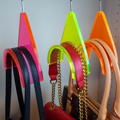 several different colored handbags hanging from hooks on a wall with chains attached to them